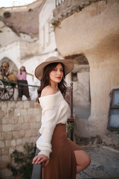 woman in white off shoulder long sleeve shirt and brown hat standing near brown concrete wall